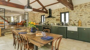 A rustic kitchen with stone walls, wooden beams, and a dining area with a wooden table and chairs.