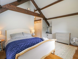 A bedroom with a bed, bedside table, lamp, dresser, mirror, and a fan. - The Ivy Barn (Abergavenny)