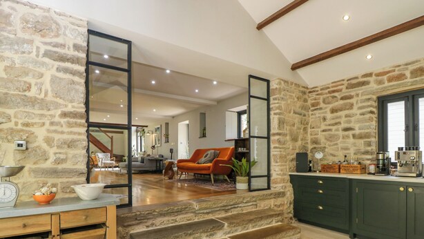A spacious kitchen with stone walls, a wooden counter, and a coffee machine.