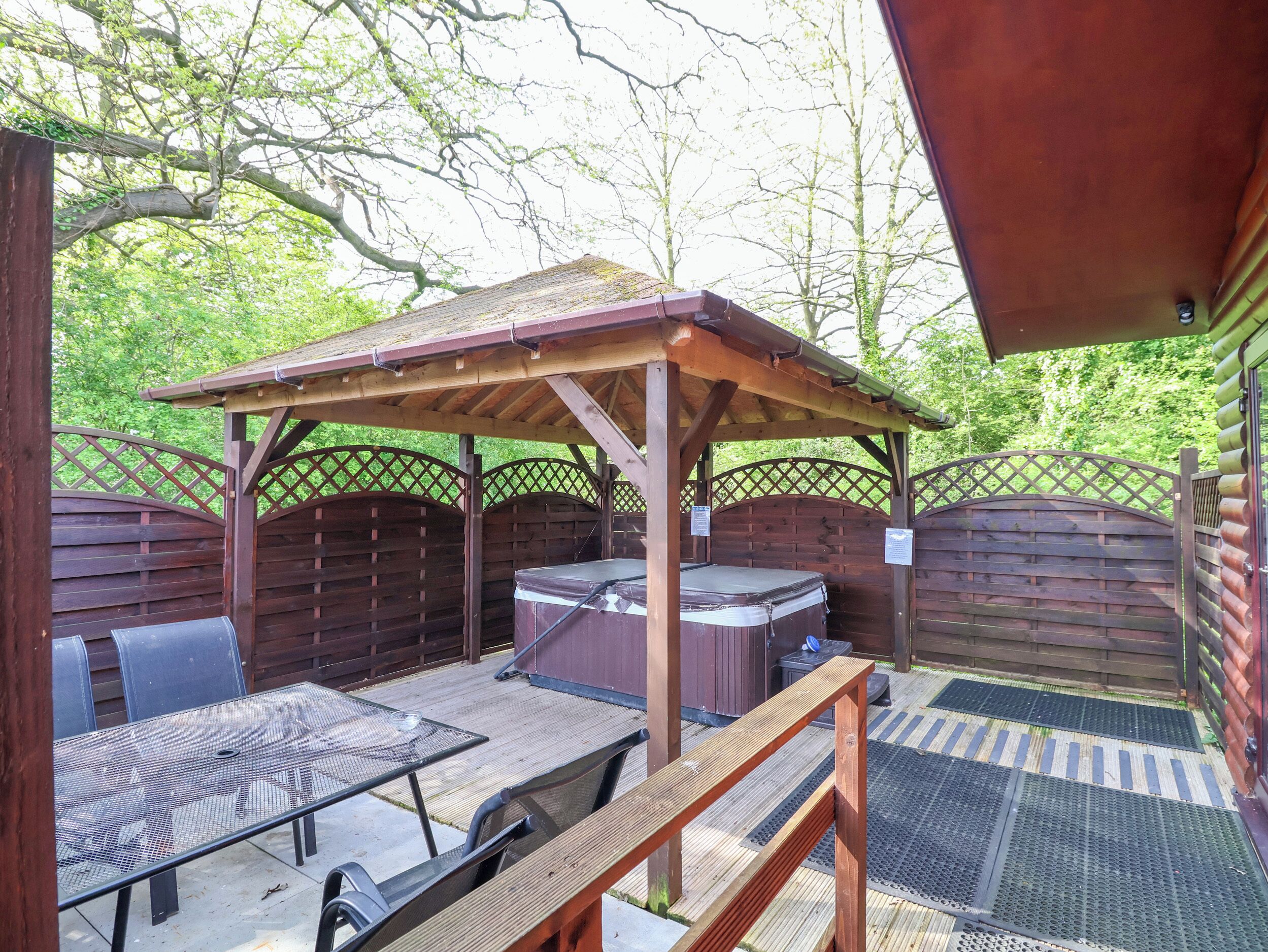 Un patio exterior con una pérgola de madera, un jacuzzi y una mesa con sillas.