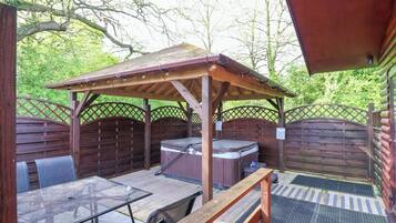 Un patio exterior con una pérgola de madera, un jacuzzi y una mesa con sillas.