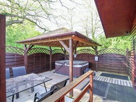 Un patio exterior con una pérgola de madera, un jacuzzi y una mesa con sillas.