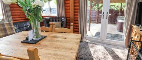 Una mesa de comedor de madera con sillas, un jarrón de flores y vistas al exterior a través de puertas de cristal.