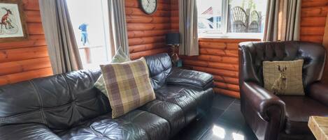 A log cabin interior with a leather sofa, a leather armchair, and a wooden dining table.