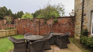 A patio with wicker furniture, a brick wall, and a wooden fence. - Low Moor (Saltburn-by-the-Sea)