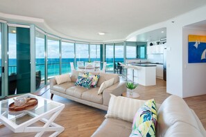 Un interior moderno con sala de estar, cocina y puertas de vidrio grandes que dan a un balcón con vista al océano.