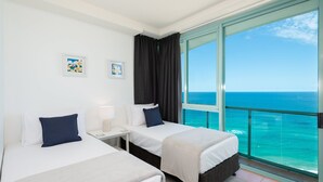 Une chambre d’hôtel avec deux lits, une table de chevet, une fenêtre donnant sur l’océan et deux tableaux encadrés au mur.