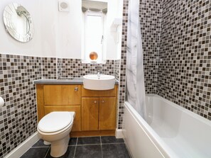 A bathroom with a toilet, sink, and bathtub, featuring mosaic tile walls and a wooden vanity. - 19 Stablefield Way (Great Yarmouth)