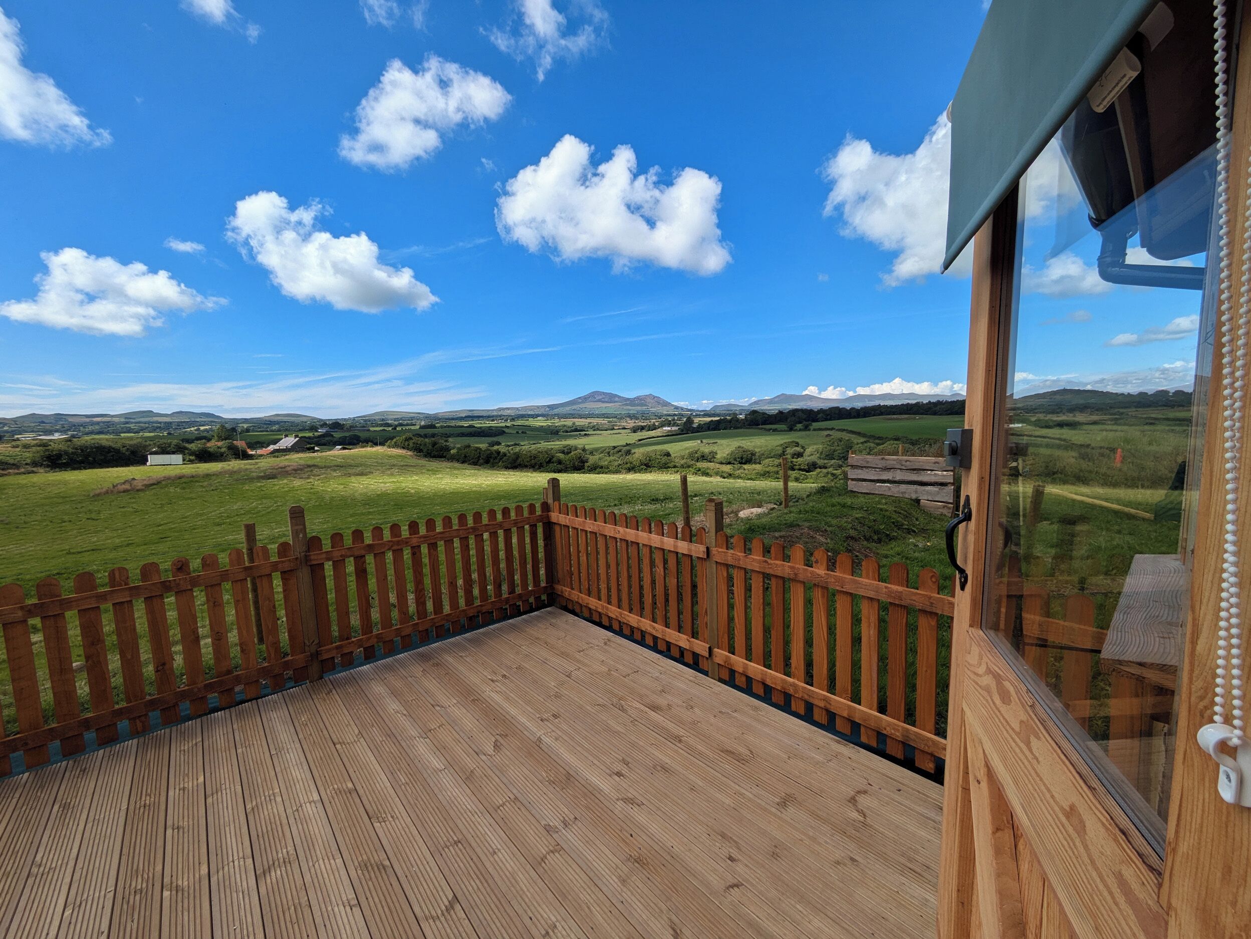 A wooden deck with a view of a green field and distant mountains.