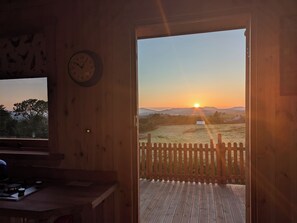 Un interno in legno con una sveglia, una scrivania e vista su un campo al tramonto.