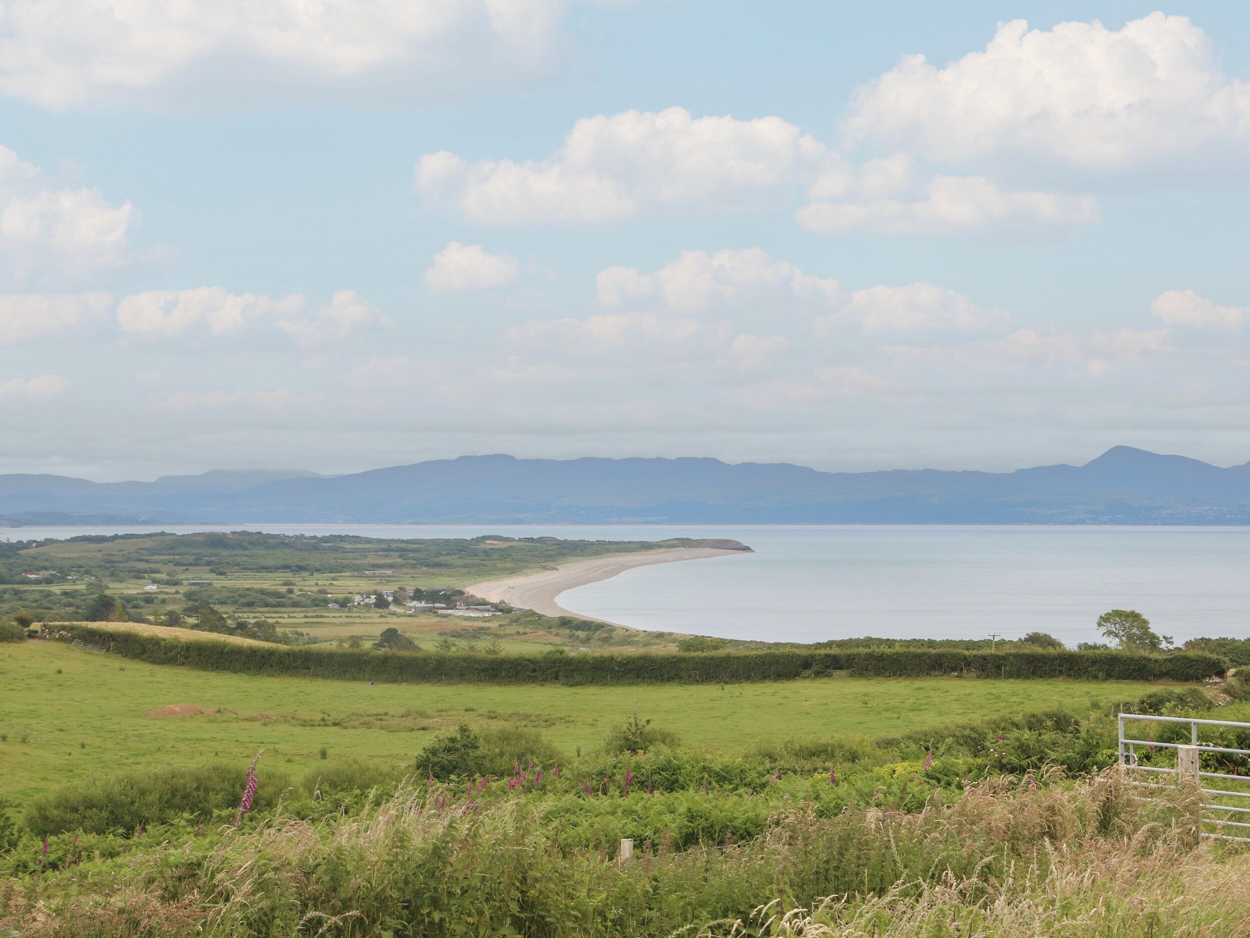 A coastal landscape with a beach, grassy fields, and distant mountains.