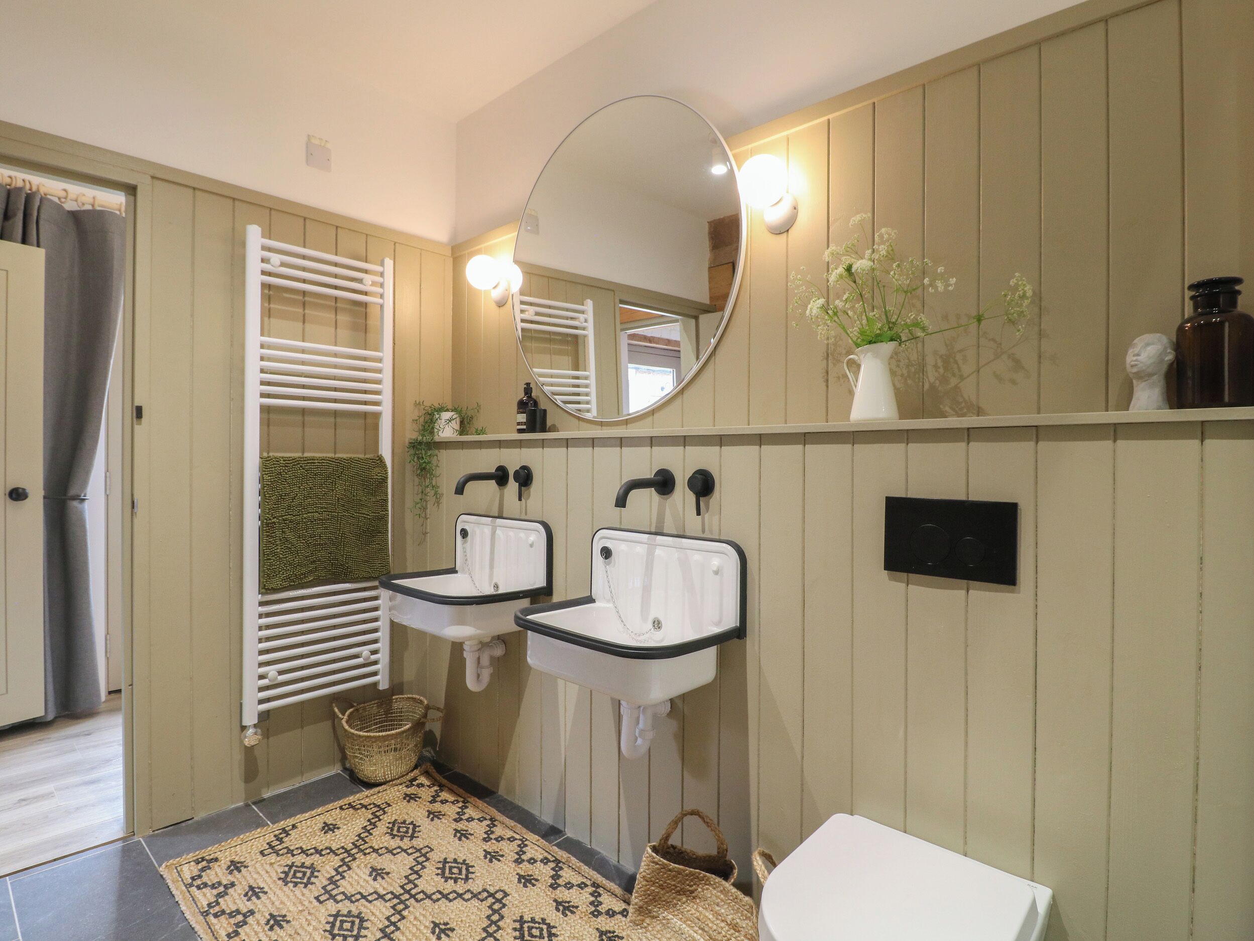 A bathroom with two sinks, a mirror, a towel rack, a basket, and a small potted plant.