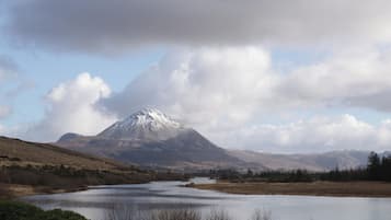 Een berg met een besneeuwde top, een rivier op de voorgrond en een bewolkte lucht.