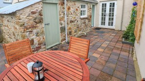A stone building with a green door, a white window, and a white door. There is a round wooden table with two chairs and a coffee pot. - Orielton Cottage (Newport)