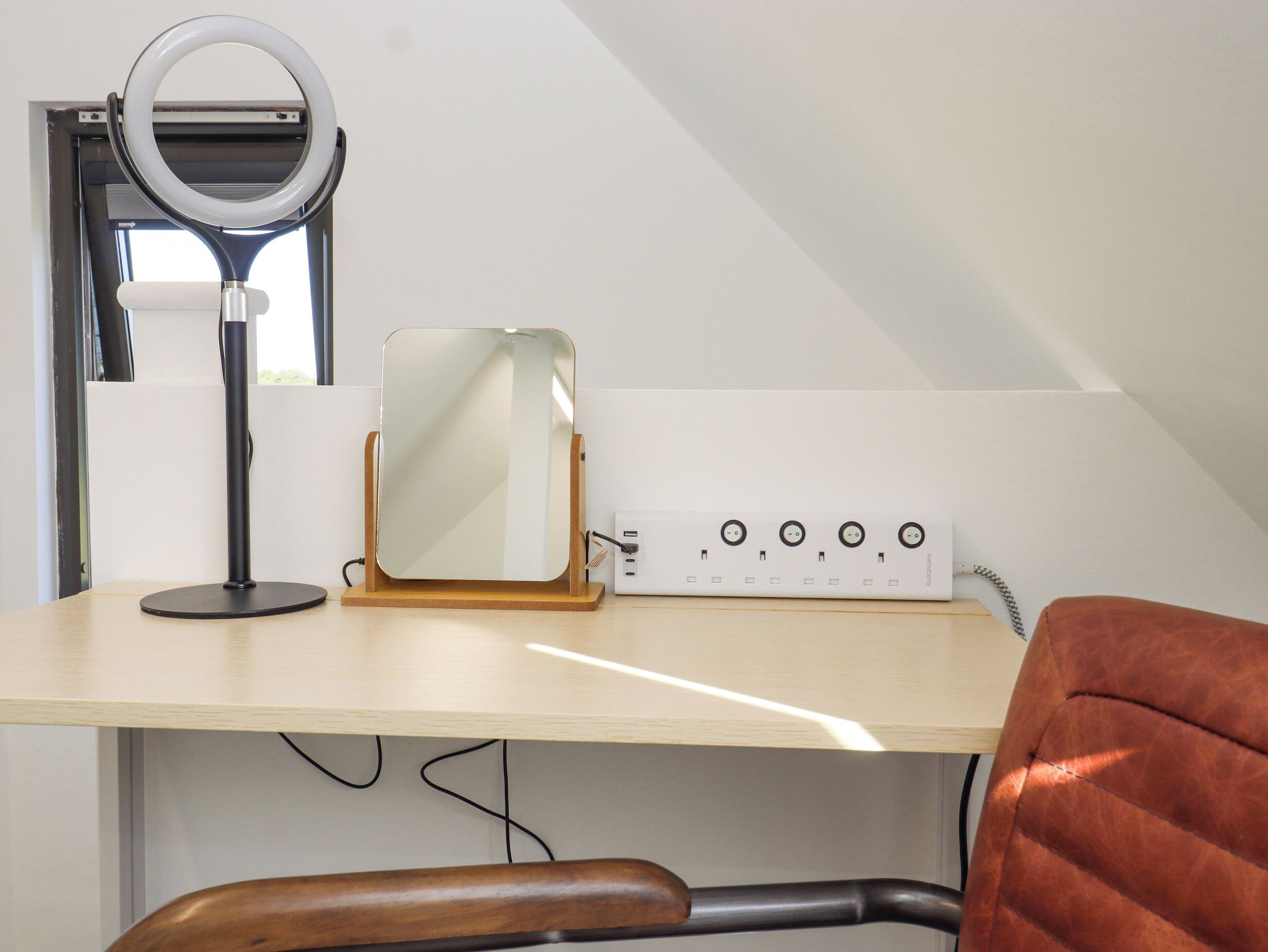 A room with a desk, a ring light, a mirror, and a power strip with multiple outlets.