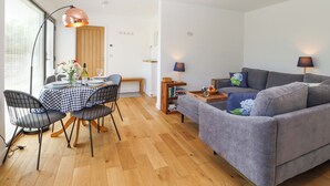 Ein modernes Wohnzimmer mit einem grauen Sofa, einem Esstisch mit Stühlen und einem Bücherregal.