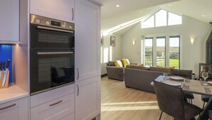 Une cuisine moderne équipée de deux fours, un coin repas avec une table pour quatre personnes, et un salon avec un canapé et une vue sur l’extérieur.