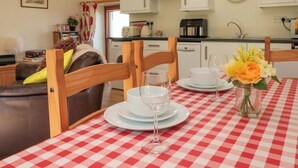 Un'area pranzo con tovaglia a quadri, sedie di legno, un vaso con fiori e una cucina sullo sfondo.
