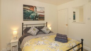 Una camera da letto con un letto, un comodino, una lampada, una porta e una parete con un quadro.