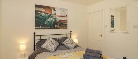 A bedroom with a bed, a nightstand, a lamp, a door, and a wall with a picture.