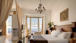 Ett hotellrum med en stor säng, en kristallkrona, utsikt över havet och en sänggavel i trä.