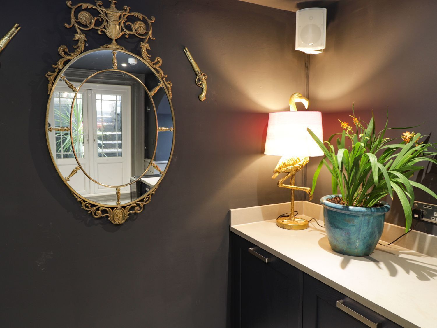 Baño con espejo redondo, lámpara y planta en maceta.