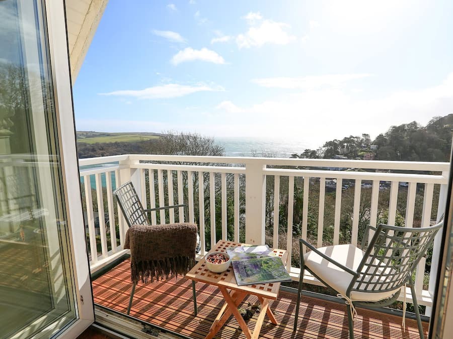 A balcony with two chairs, a small table, and a view of the sea.