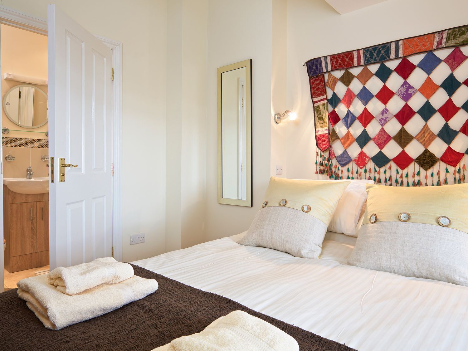A hotel room with a bed, a mirror, a quilted headboard, and a bathroom visible through an open door.