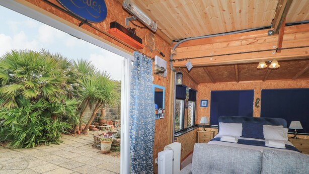 A cozy room with a bed, bedside tables, and a view of a garden with plants and a wooden deck. - The Games Room (Chichester)