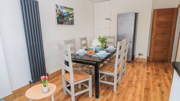 Un comedor con una mesa lista para cuatro personas, sillas, una mesita auxiliar con un jarrón y un refrigerador al fondo.