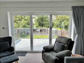 A room with a sliding glass door leading to a patio, a black armchair, a striped armchair, and a small wooden table. - The Swanage Rail Lookout (Swanage)