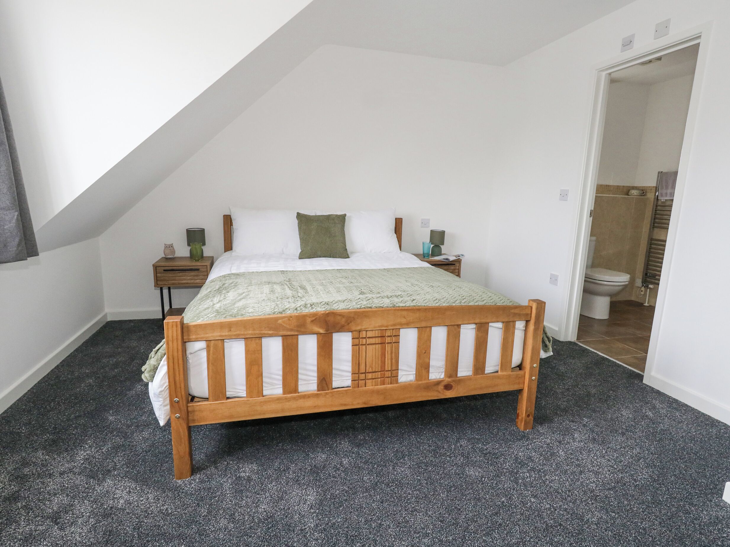 Un dormitorio con una cama de madera, una mesita de noche, una lámpara y un cojín verde.