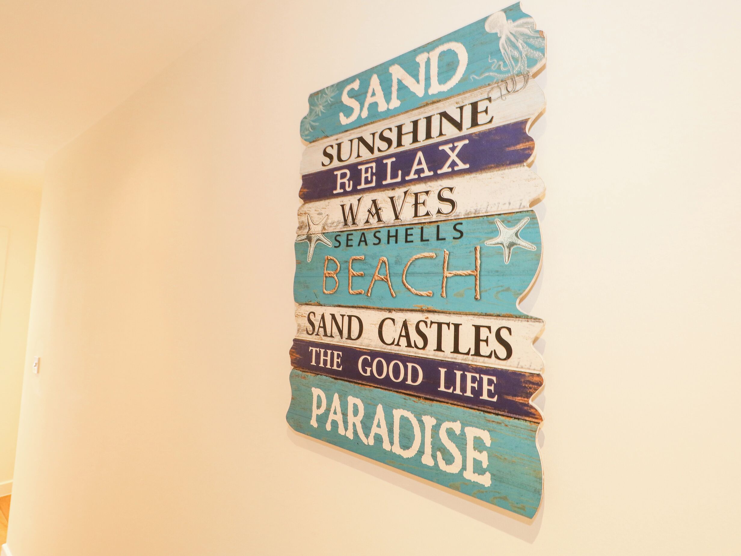 Un cartello appeso al muro con scritte come 'SABBIA', 'SOLE' e 'PARADISO'.