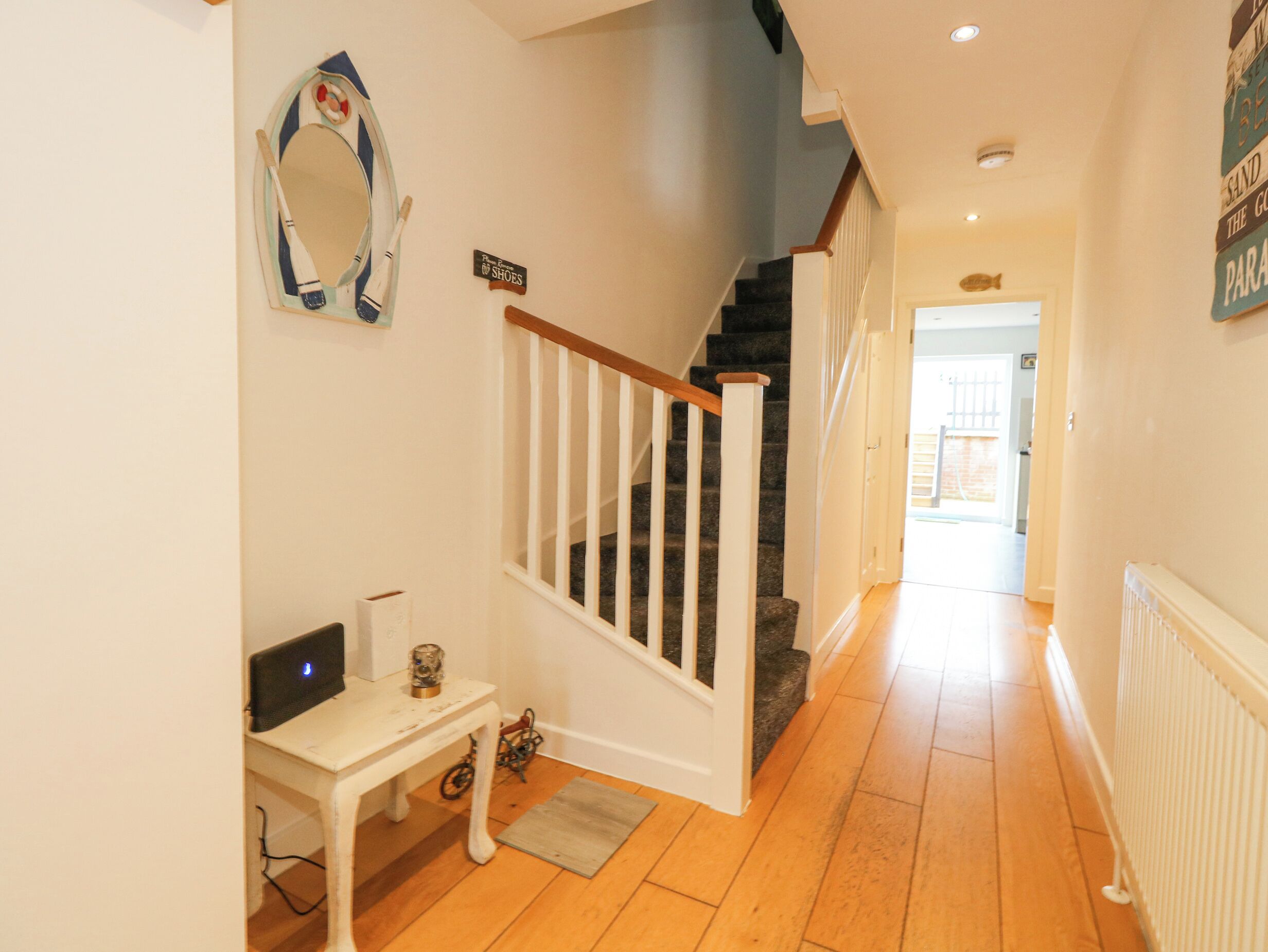 A hallway with a staircase, a white table with a computer, and a mirror on the wall.