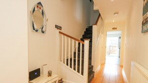 A hallway with a staircase, a white table with a computer, and a mirror on the wall. - Dotties Retreat (Weymouth)