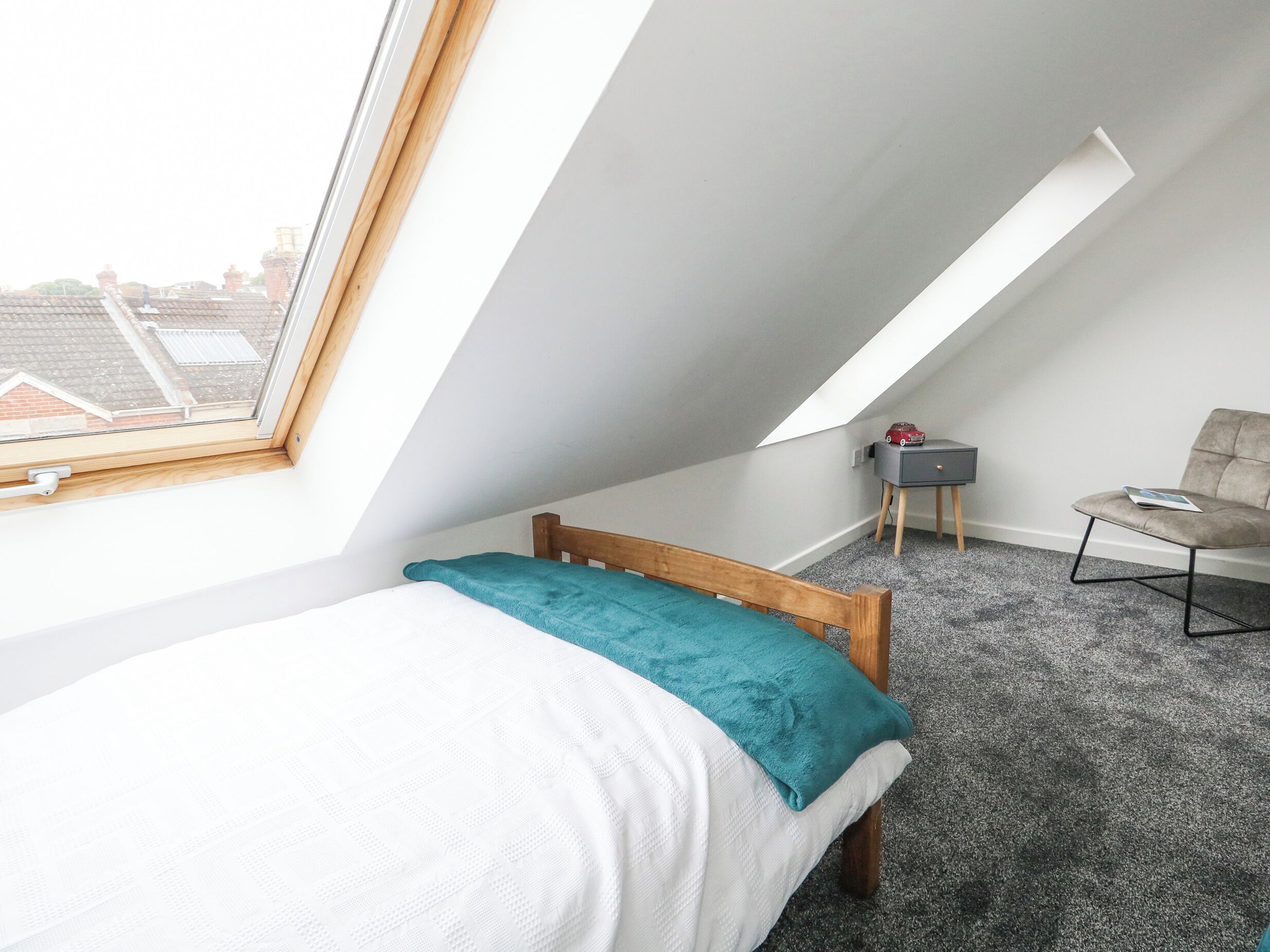 Ein kleines, modernes Schlafzimmer mit schrägem Dach, einem Einzelbett, einem Sessel und einem kleinen Tisch.