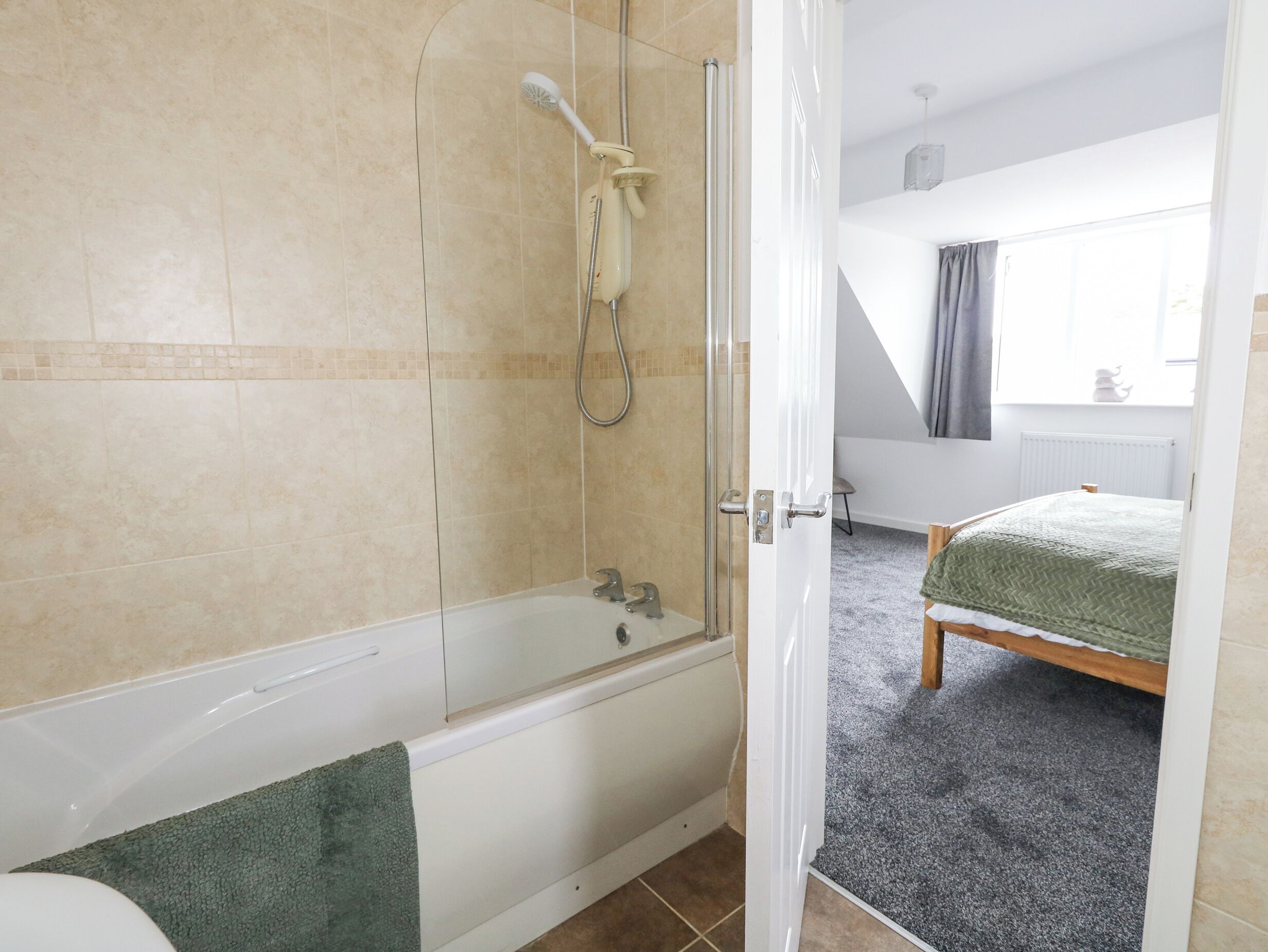 A modern bathroom with a bathtub, shower, and a visible door leading to a bedroom.