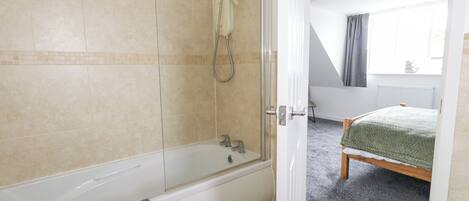 A modern bathroom with a bathtub, shower, and a visible door leading to a bedroom.