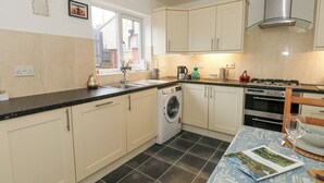 A modern kitchen with a washing machine, stove, oven, and a dining area with a table set for two. - Dotties Retreat (Weymouth)
