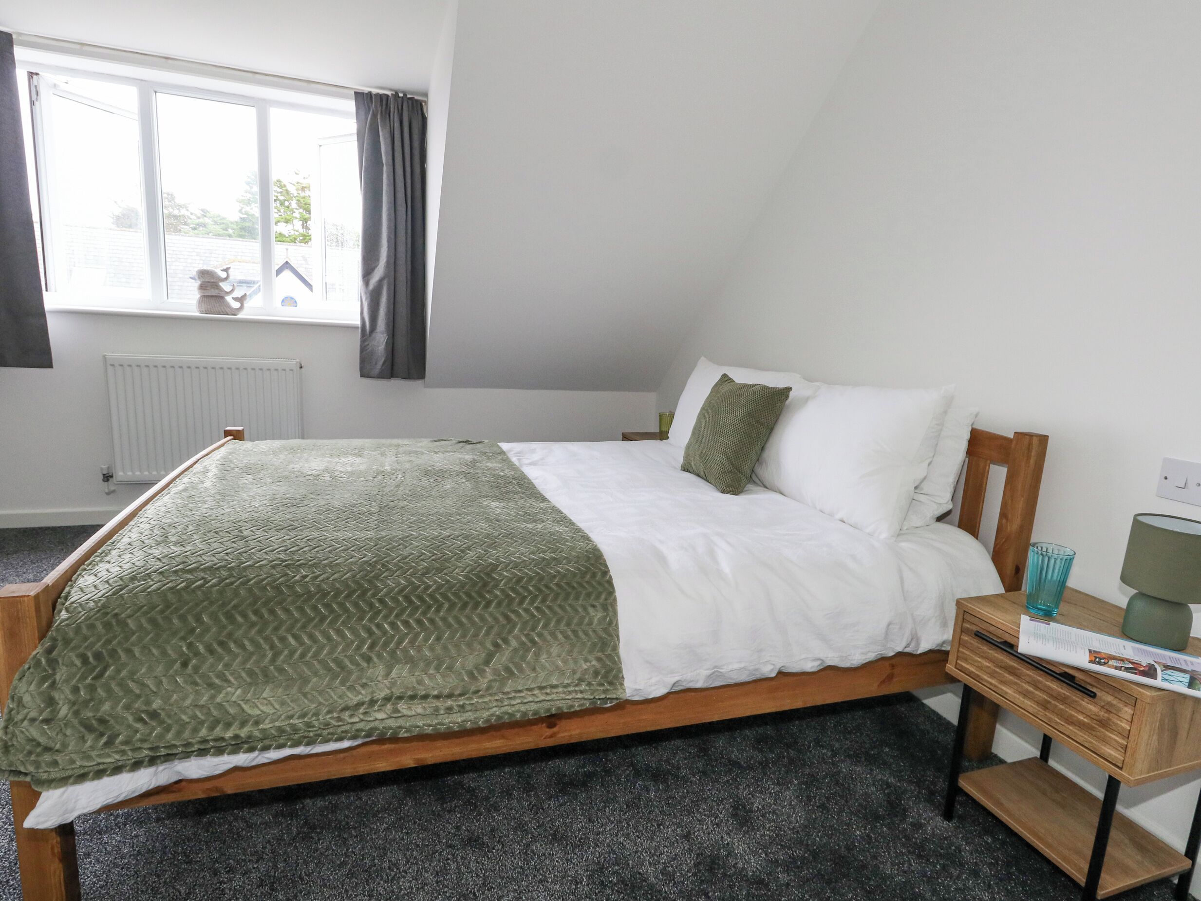 Een slaapkamer met een bed, een houten nachtkastje, een raam met gordijnen en een radiator.