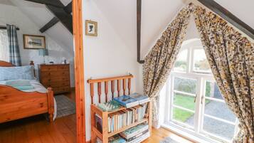Une chambre confortable avec un lit en bois, une bibliothèque et une fenêtre agrémentée de rideaux à motifs.