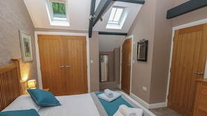 Een slaapkamer met een bed, twee houten deuren, een dakraam en een spiegel aan de muur.