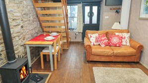 Een knus ingerichte kamer met een open haard, houten meubels, een bank met kerstkussens en een stenen muur.