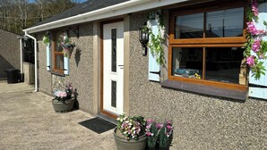 A building with a stone facade, a wooden-framed window, and a door. There are potted plants and a wall-mounted light fixture. - The Mill (Pwllheli)
