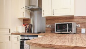 A kitchen with white cabinets, a stainless steel range hood, a microwave, and wooden countertops. - The Mill (Pwllheli)