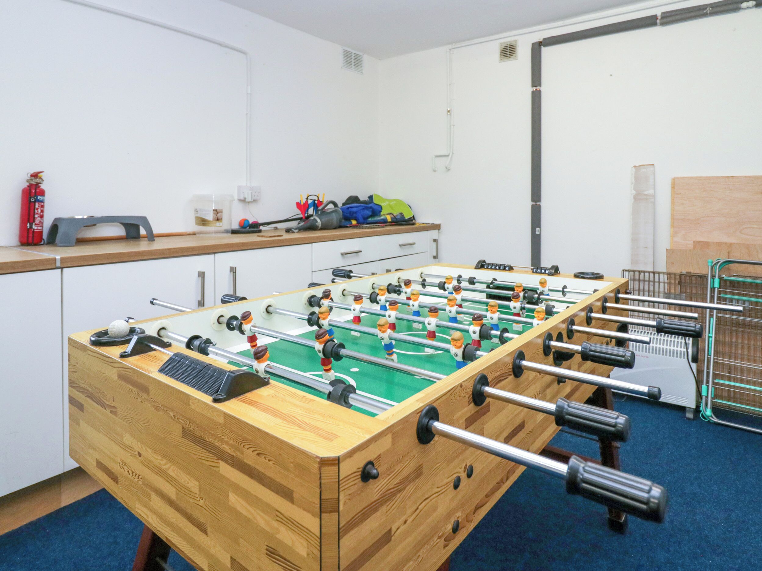 A foosball table in a room with a blue carpet, wooden cabinets, and a fire extinguisher on the wall.