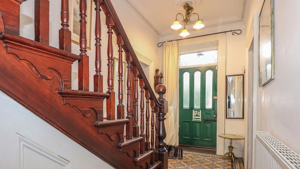 A wooden staircase with a fire exit sign, a green door, and a patterned floor. - Plas Dorothea (Caernarfon)