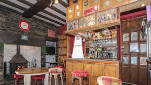 A rustic pub interior with a wooden bar, stools, a stone wall, a fireplace, and a clock. - Plas Dorothea (Caernarfon)