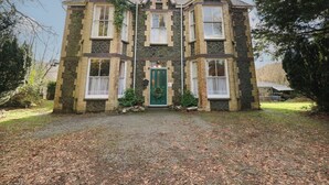 A two-story stone building with a green door, multiple windows, and a gravel driveway. - Plas Dorothea (Caernarfon)