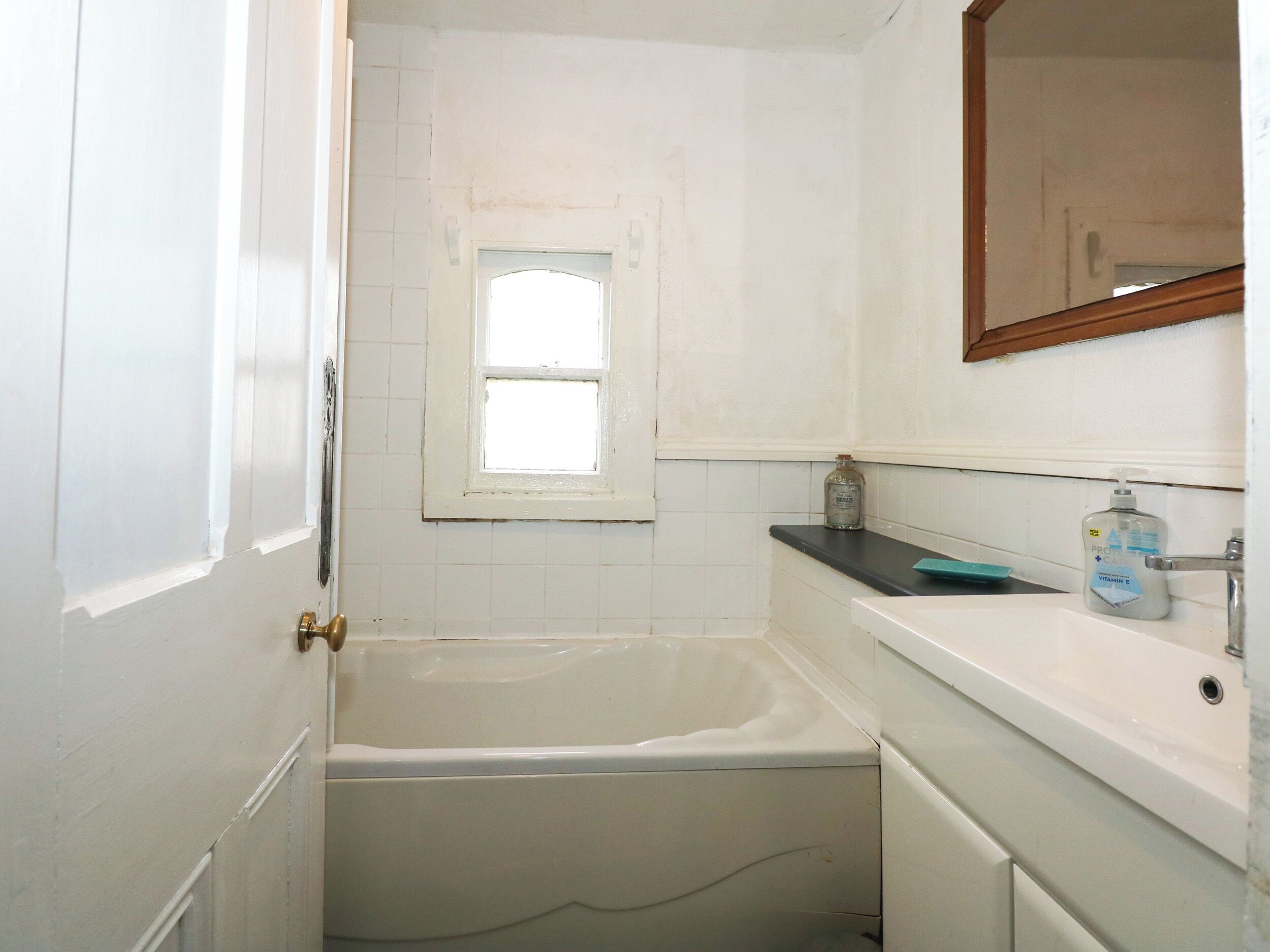 Ein Badezimmer mit einer Badewanne, einem Fenster, einem Waschbecken und einem Spiegel.
